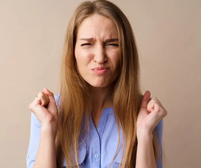 Young woman pulls a face with raised hands and slightly clenched fists.